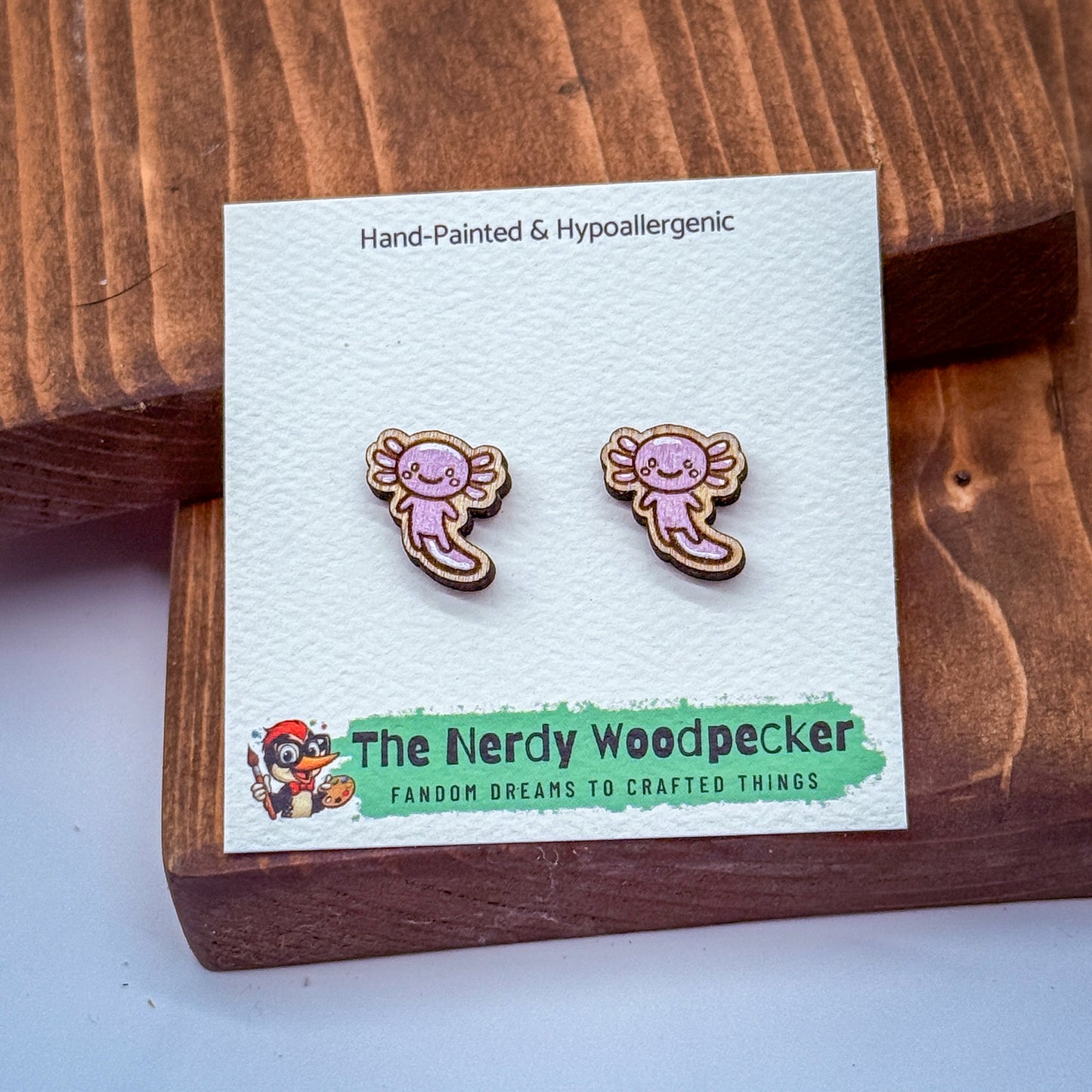 a pair of hand-painted wooden earrings with a cute cartoon character design, placed on a wooden surface.