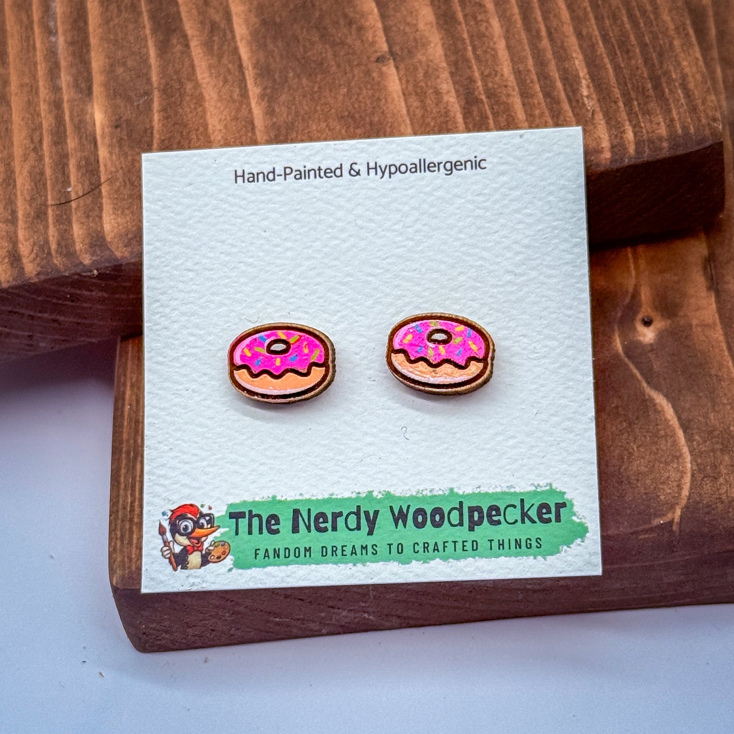 a pair of hand-painted and hypoallergenic earrings in the shape of donuts, displayed on a wooden surface.