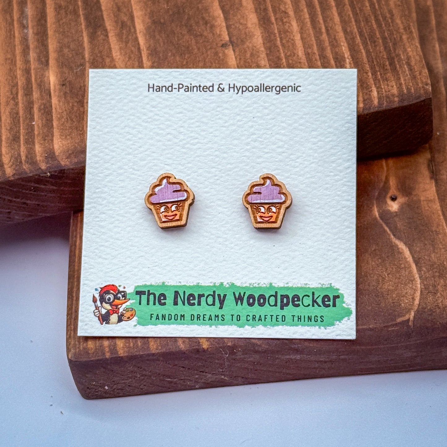 A pair of hand-painted and hypoallergenic earrings in the shape of cupcakes, displayed on a wooden surface.