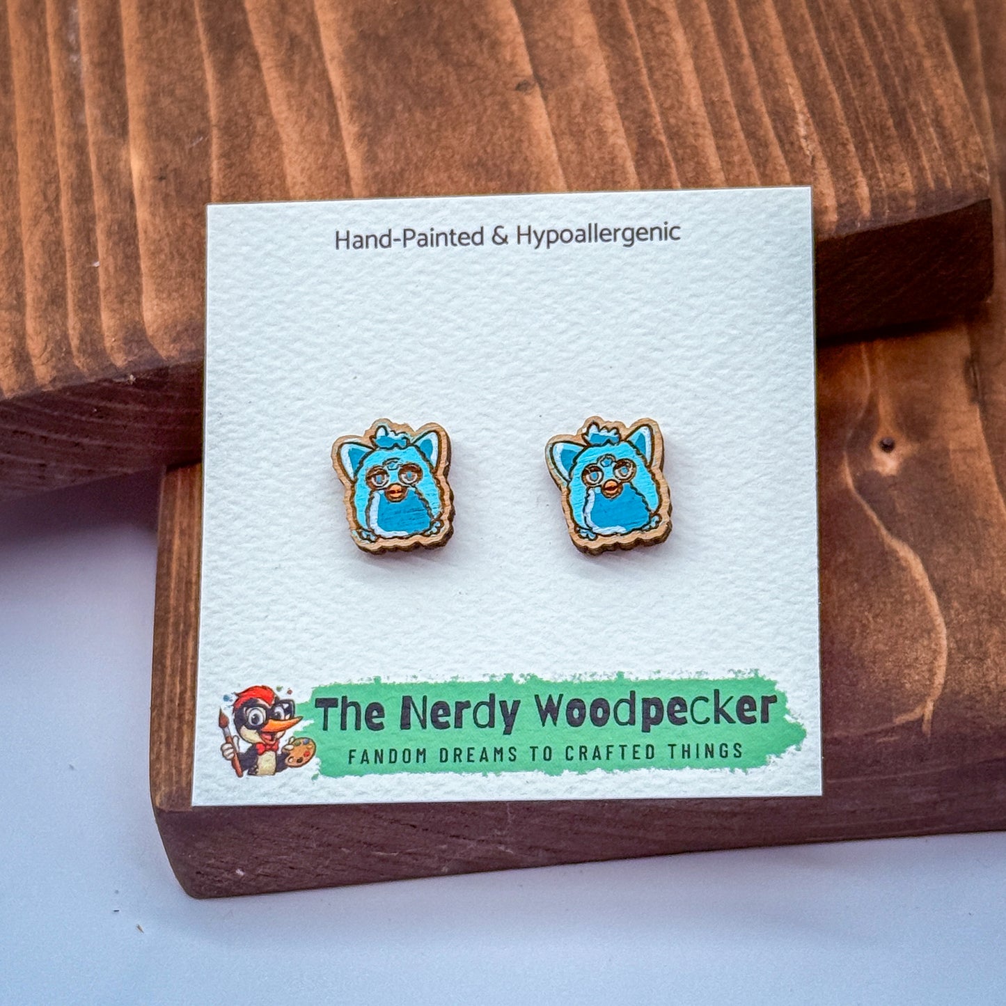 a pair of earrings with blue and white cartoon-like faces, placed on a wooden surface.