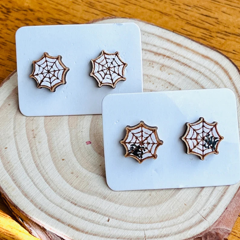 three wooden earrings with spider web designs, placed on a wooden surface.