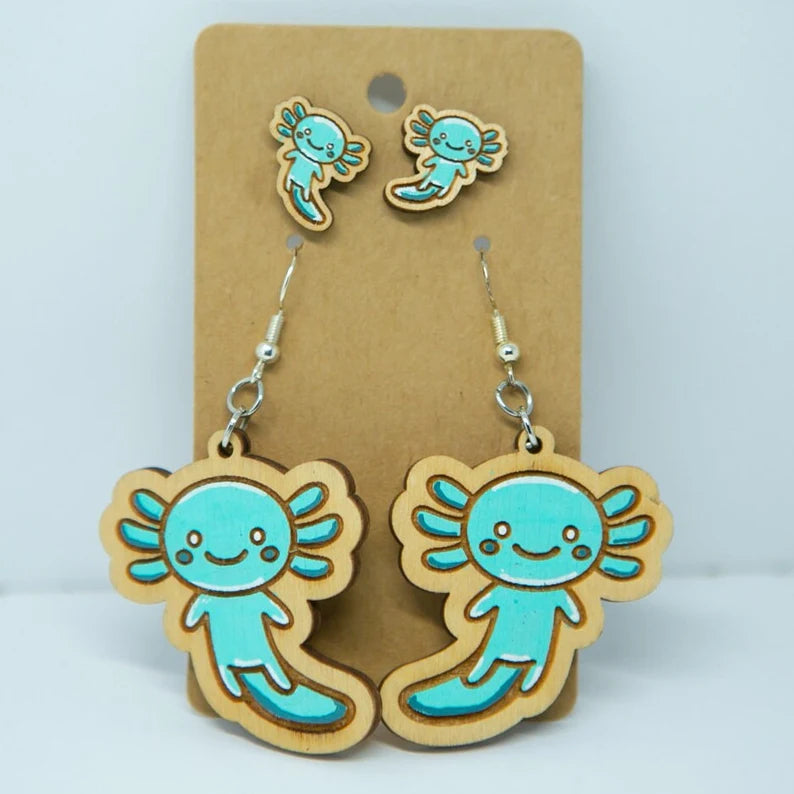 A pair of wooden earrings featuring cartoon axolotl characters, which are small aquatic salamanders.