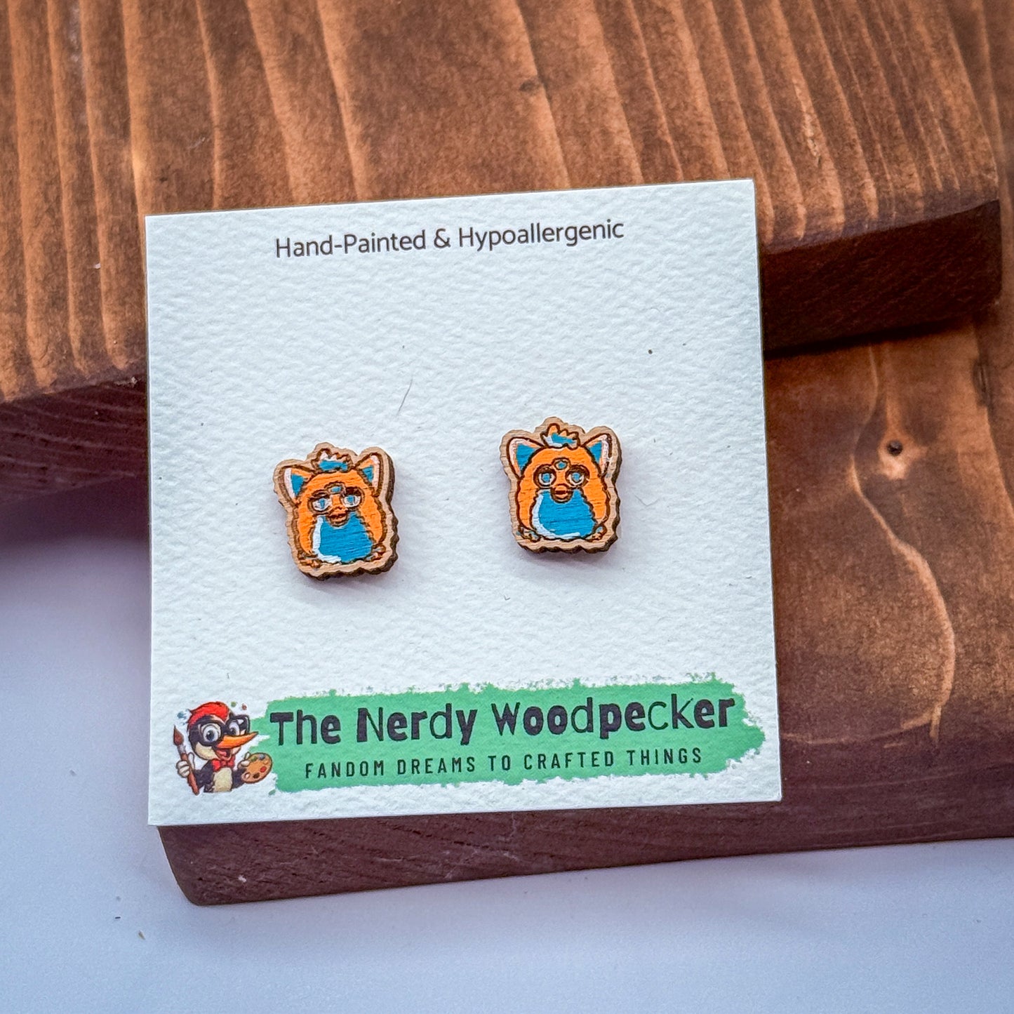 a pair of earrings made of wood, with a wooden board and a white card with text and an illustration of a wooden character.