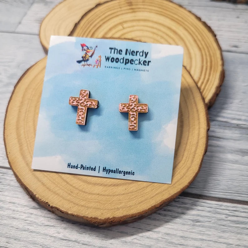 a pair of hand-painted hypoallergenic earrings in the shape of a cross, displayed on a wooden coaster.