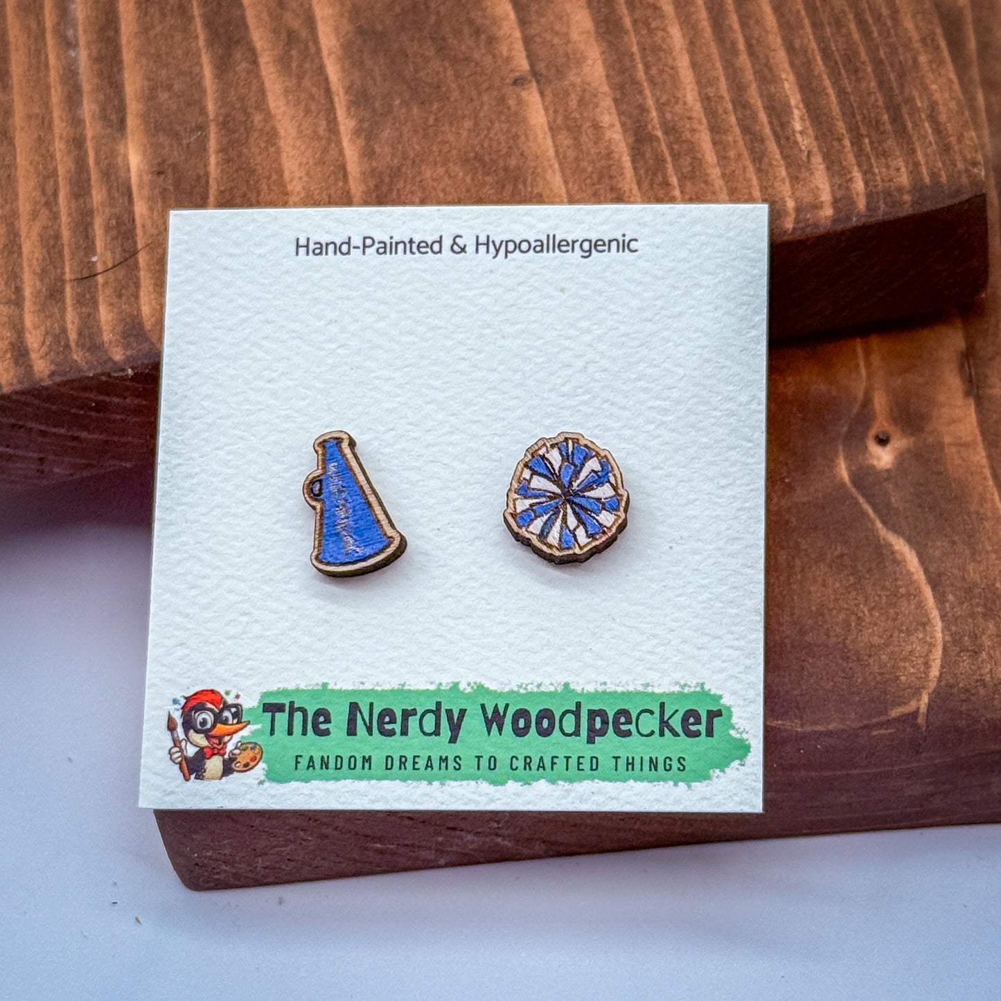 a pair of earrings, one in blue and the other in gold, displayed on a white card with text and a cartoon character.