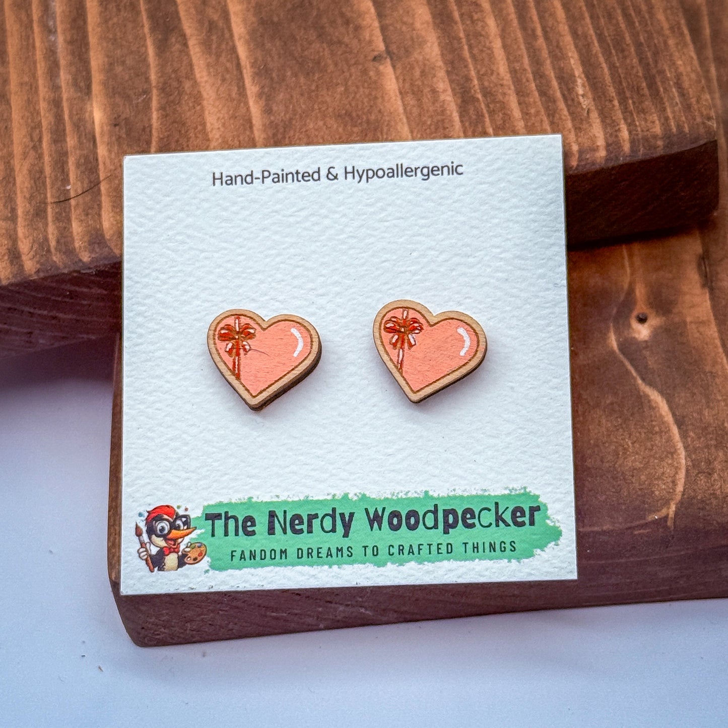 a pair of earrings made of wood, with a wooden background and a white card with text and an illustration.