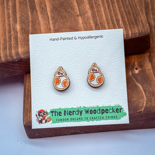 a pair of hand-painted and hypoallergenic earrings in the shape of the character BB-8 from the Star Wars franchise, displayed on a wooden surface.