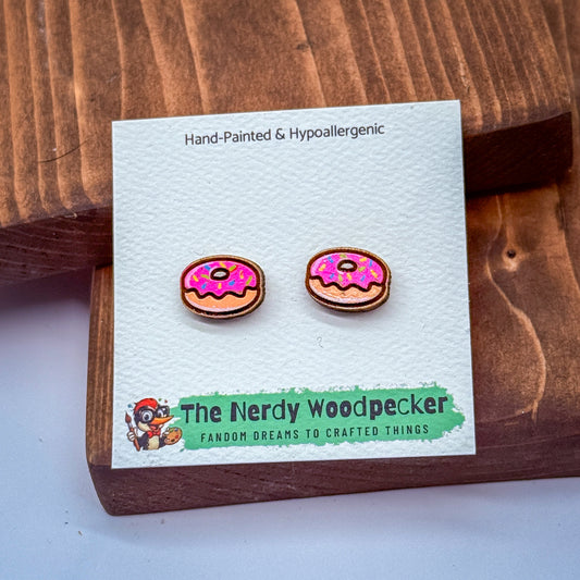 a pair of hand-painted and hypoallergenic earrings in the shape of donuts, displayed on a wooden surface.