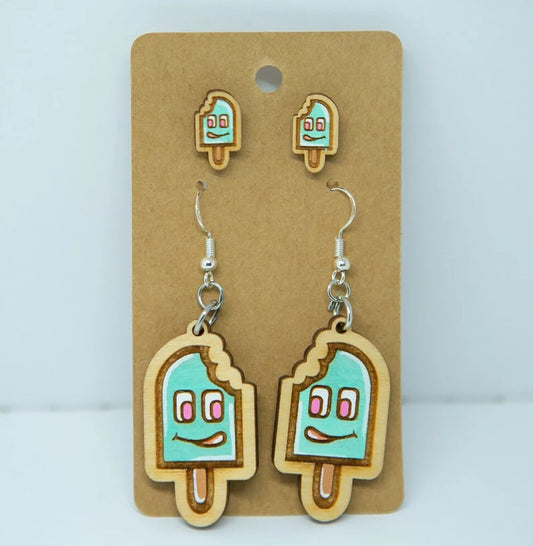 A pair of earrings featuring cartoon-style ice cream characters on a brown cardboard backing.