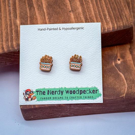 a pair of earrings displayed on a wooden surface, with a white card underneath that has text and a logo.