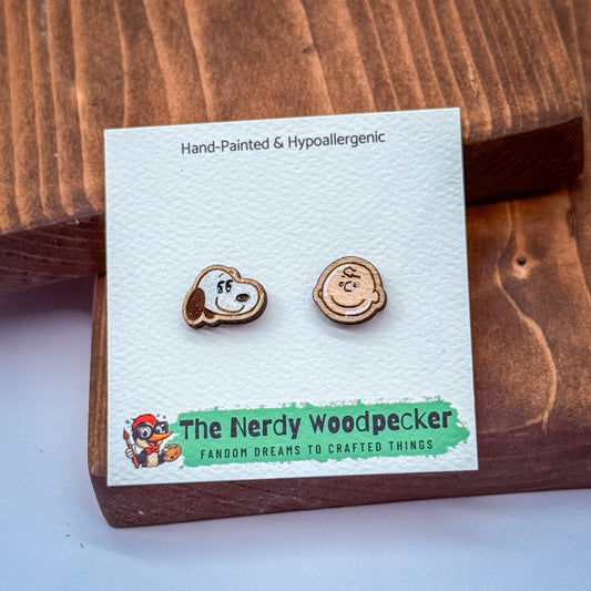 a pair of wooden earrings with cartoon-like faces, placed on a white card with text and a logo.