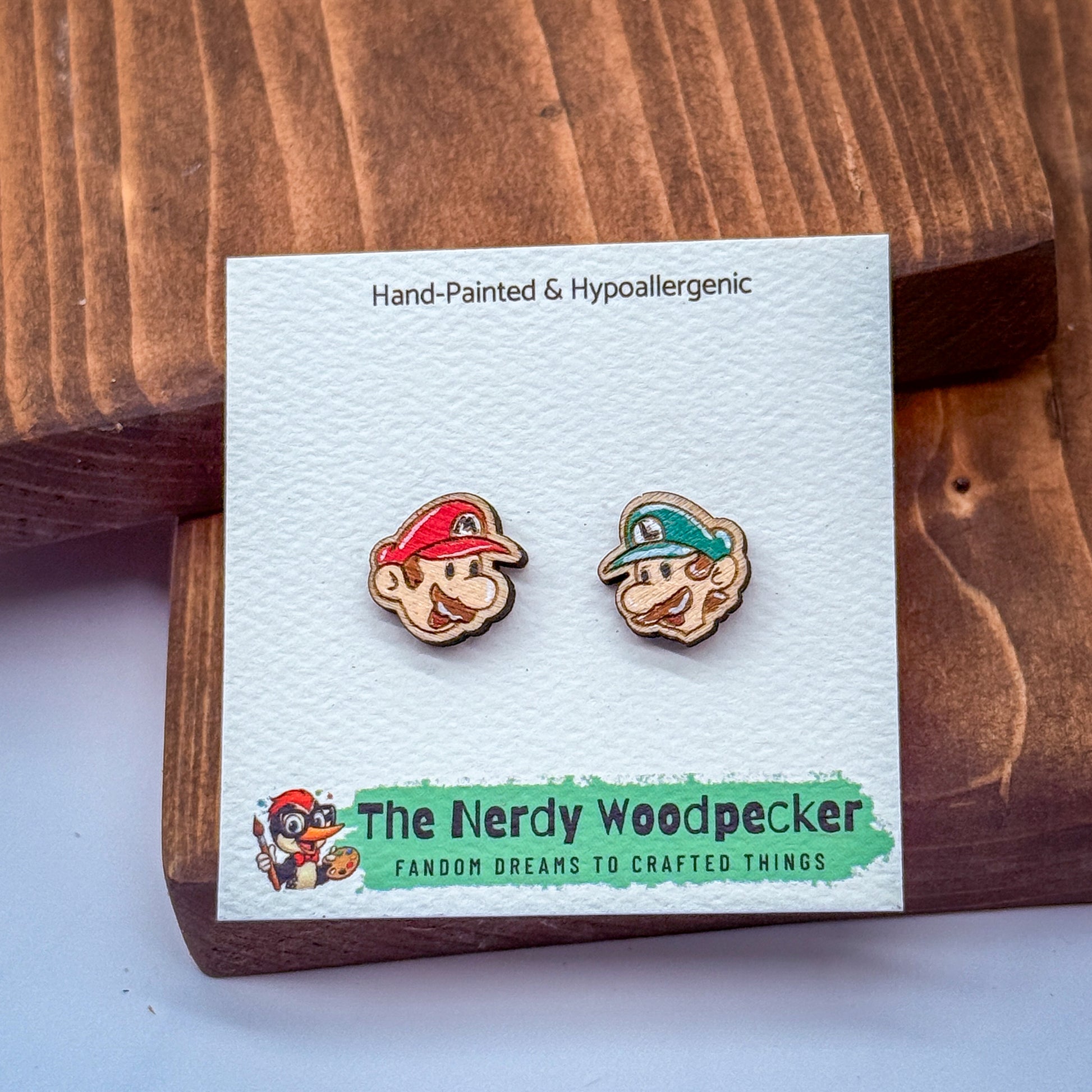 two wooden earrings with cartoon-like faces, placed on a white card with text and a logo.