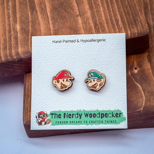 two wooden earrings with cartoon-like faces, placed on a white card with text and a logo.