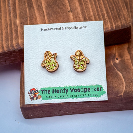 a pair of earrings with cartoon-like corn cob designs, presented on a white card with text and a logo.