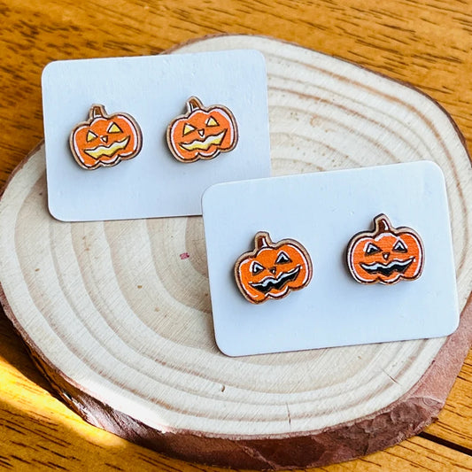 three pairs of Halloween-themed earrings, each with a pumpkin design. The earrings are displayed on a wooden surface, possibly a wooden coaster or a wooden board.