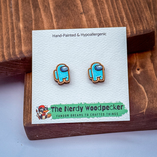 a pair of hand-painted and hypoallergenic earrings in the shape of a character from the video game "The Nerdly Woodpecker". The earrings are displayed on a wooden surface, and there is a card with text and an illustration of the character on it.