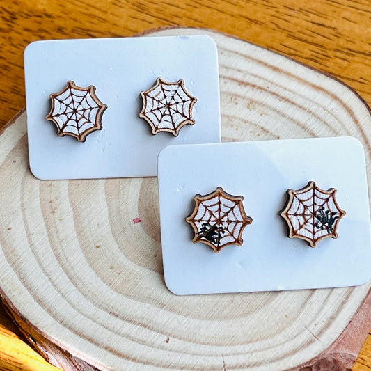 three wooden earrings with spider web designs, placed on a wooden surface.