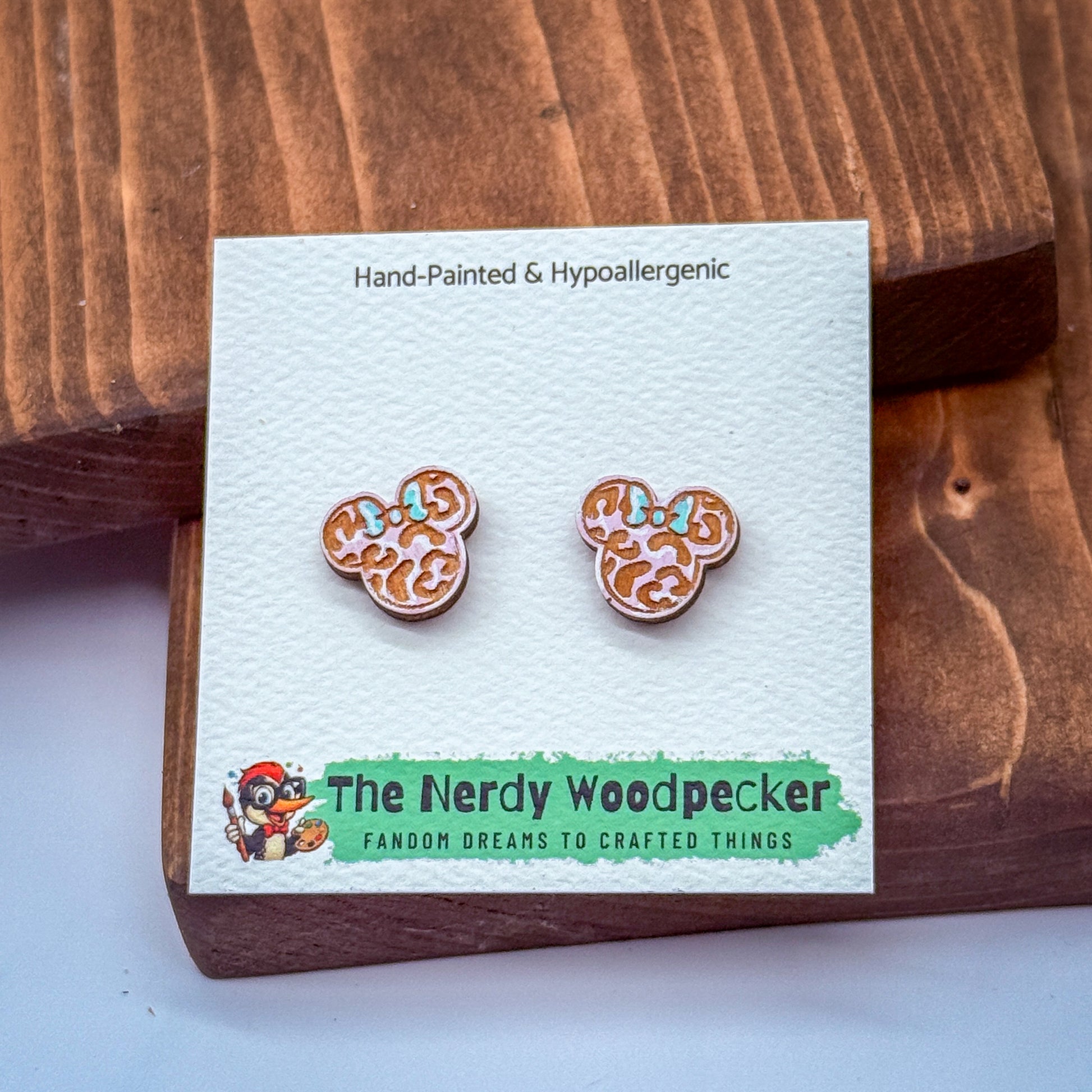 A pair of hand-painted and hypoallergenic earrings in the shape of Mickey Mouse ears, displayed on a wooden surface.