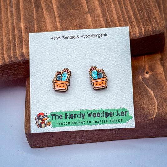 a pair of hand-painted and hypoallergenic earrings with cactus designs, displayed on a wooden surface.