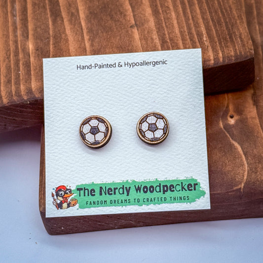 a pair of earrings with a soccer ball design, presented on a white card with text and a logo.