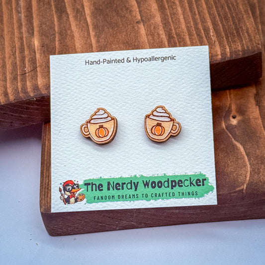 a pair of hand-painted and hypoallergenic earrings with pumpkin-shaped handles, displayed on a wooden surface.