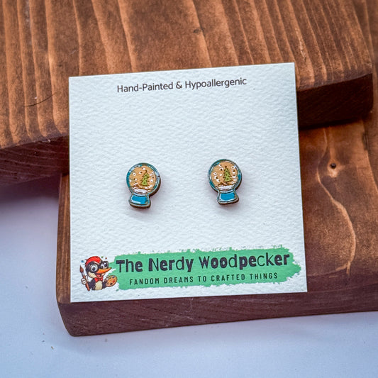 A pair of hand-painted hypoallergenic earrings with a snow globe design, presented on a wooden surface.