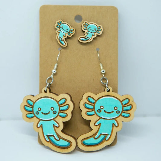 A pair of wooden earrings featuring cartoon axolotl characters, which are small aquatic salamanders.