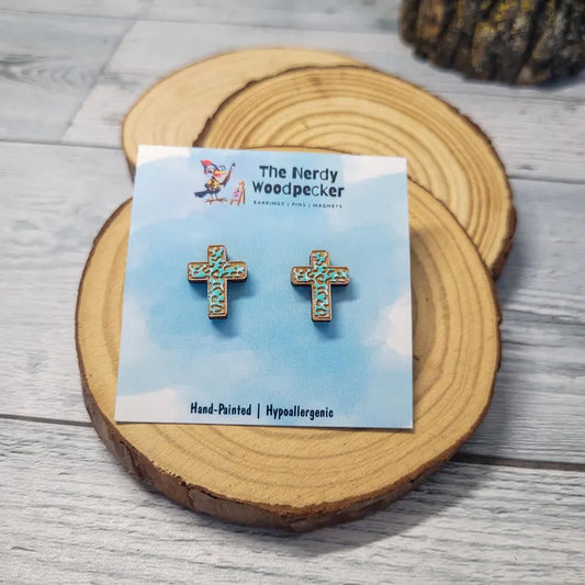 A pair of hand-painted hypoallergenic earrings in the shape of a cross, displayed on a wooden coaster.