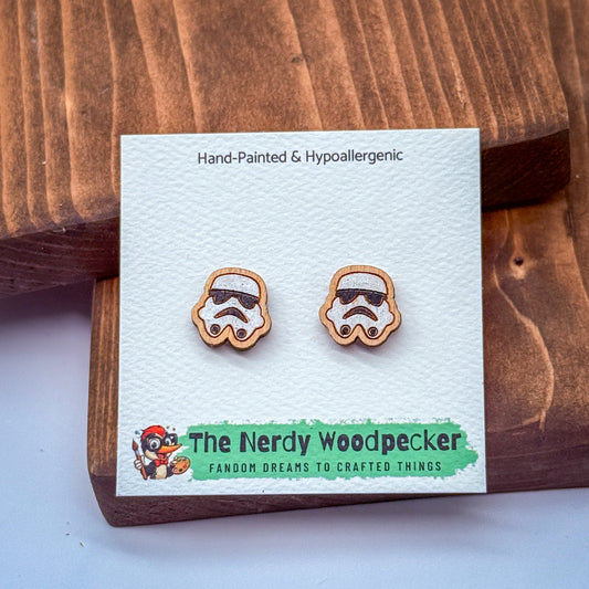 A pair of hand-painted and hypoallergenic earrings featuring stormtrooper-style icons, presented on a wooden surface.