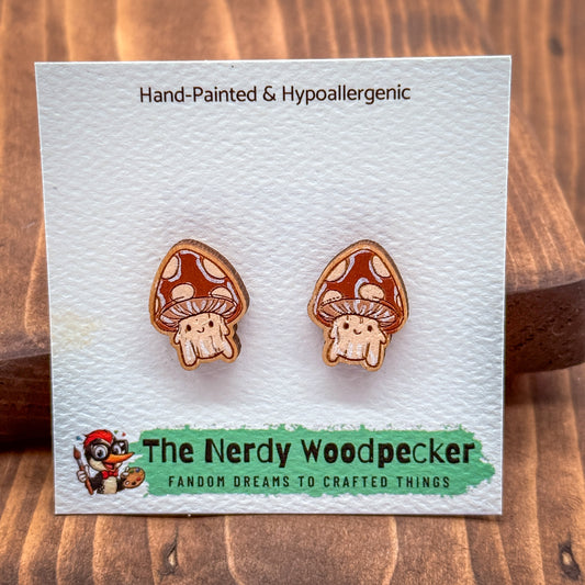 a pair of hand-painted and hypoallergenic earrings in the shape of mushrooms, presented on a white card with text and a cartoon image.