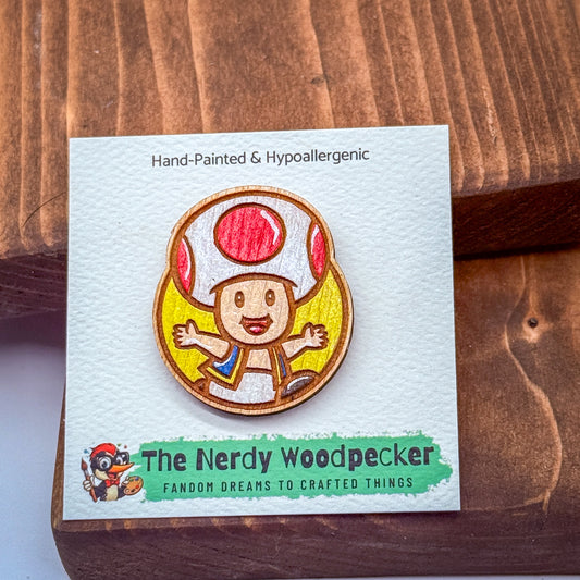 A hand-painted wooden pin featuring a cartoon character resembling a mushroom or toad, with a label indicating it is a hypoallergenic product.