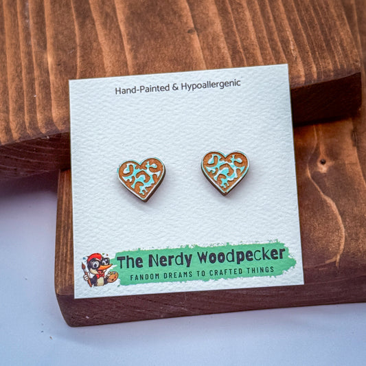 a pair of earrings with a heart-shaped design, placed on a wooden surface. The earrings are presented on a white card with text and a cartoon character.