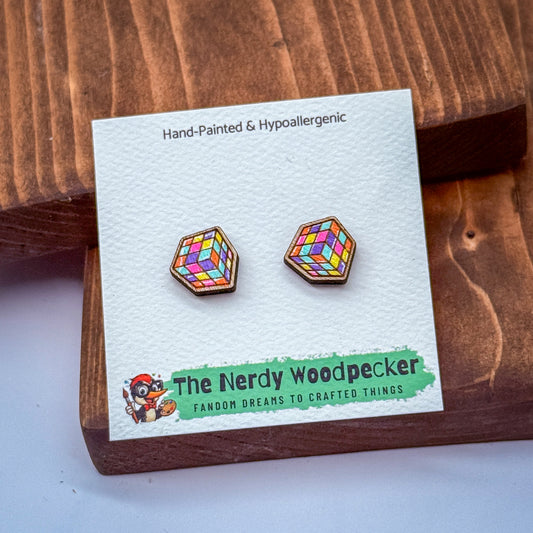 a pair of earrings with a colorful geometric design, placed on a wooden surface. The earrings are presented in a white card with text and a logo.