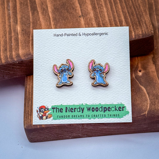 A pair of hand-painted and hypoallergenic earrings featuring a character from the "Stitch" movie franchise, displayed on a wooden surface.