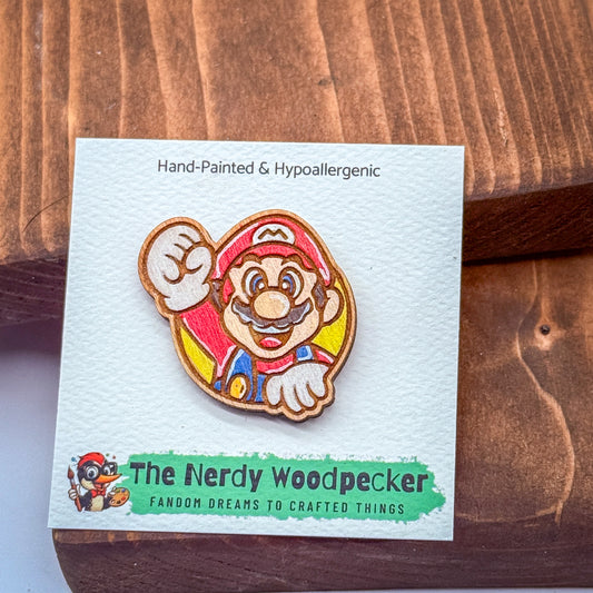 A hand-painted and hypoallergenic pin of Mario, the iconic character from the Super Mario video game franchise, is displayed on a wooden surface.